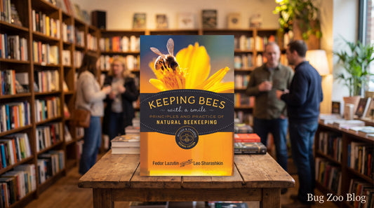 Natural beekeeping guidebook standing on a wooden table in a bookstore, cover showing a bee on a bright yellow flower with people browsing in the softly blurred background and “Bug Zoo Blog” in the lower right.